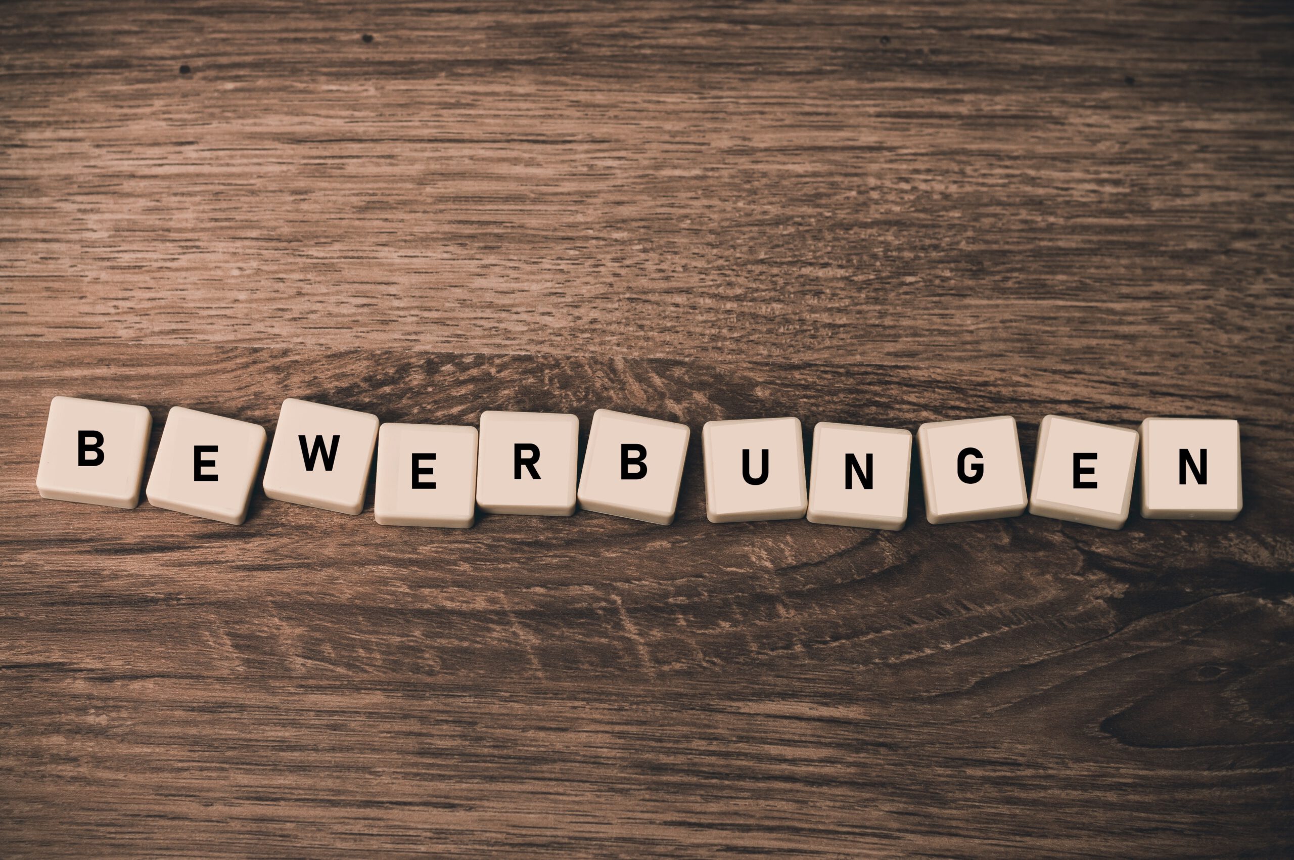 Holzbuchstaben auf einem Tisch ergeben das Wort Bewerbungen